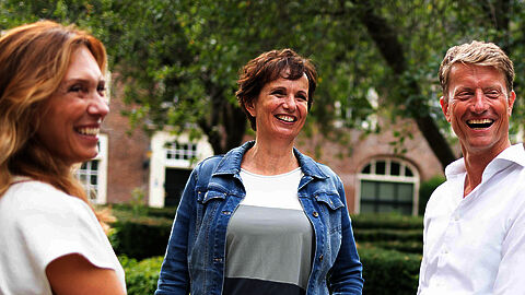 Drie collega's poseren in tuin en lachen